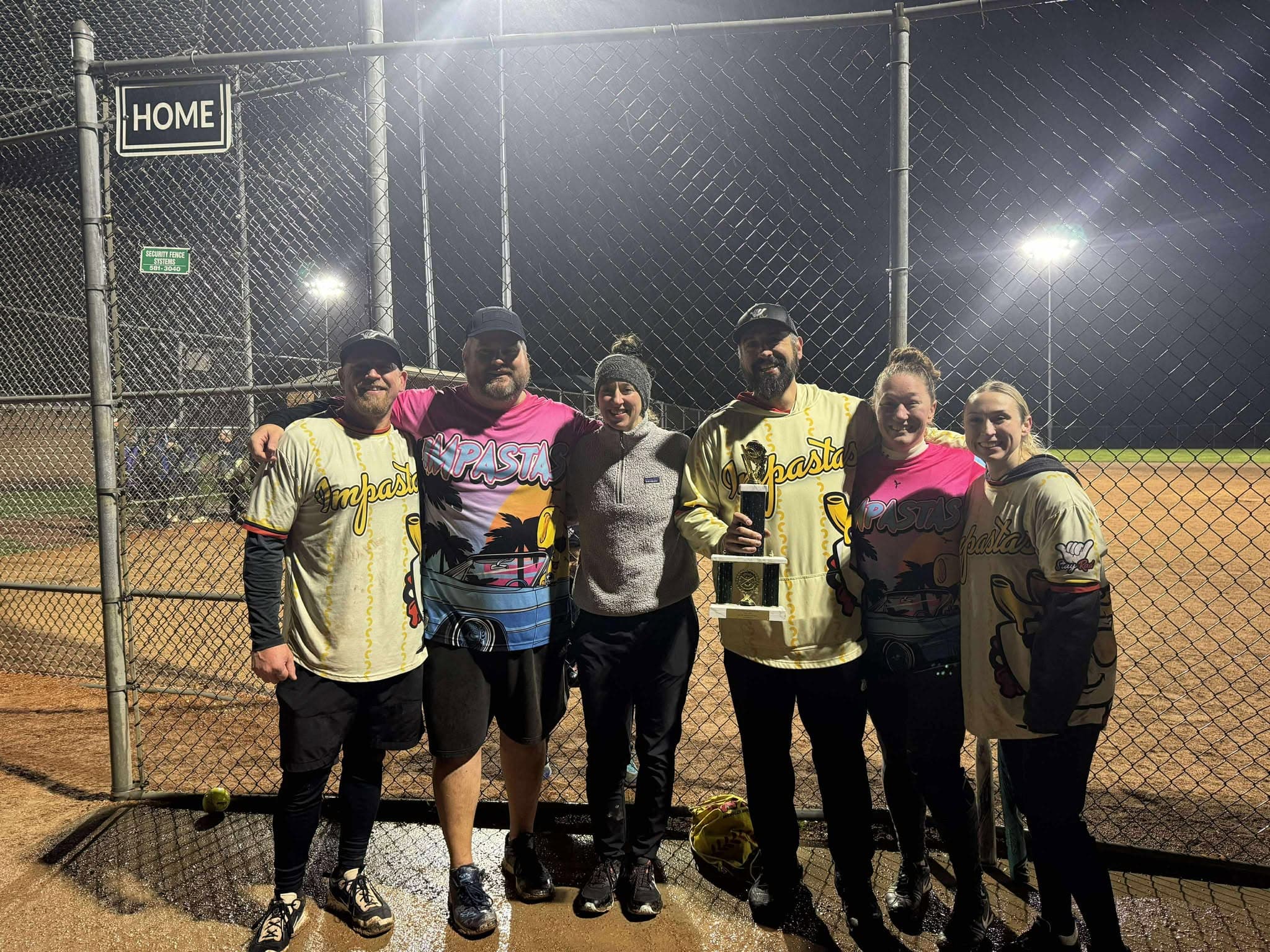 Six Impastas players with the championship trophy by the home gate under the field lights