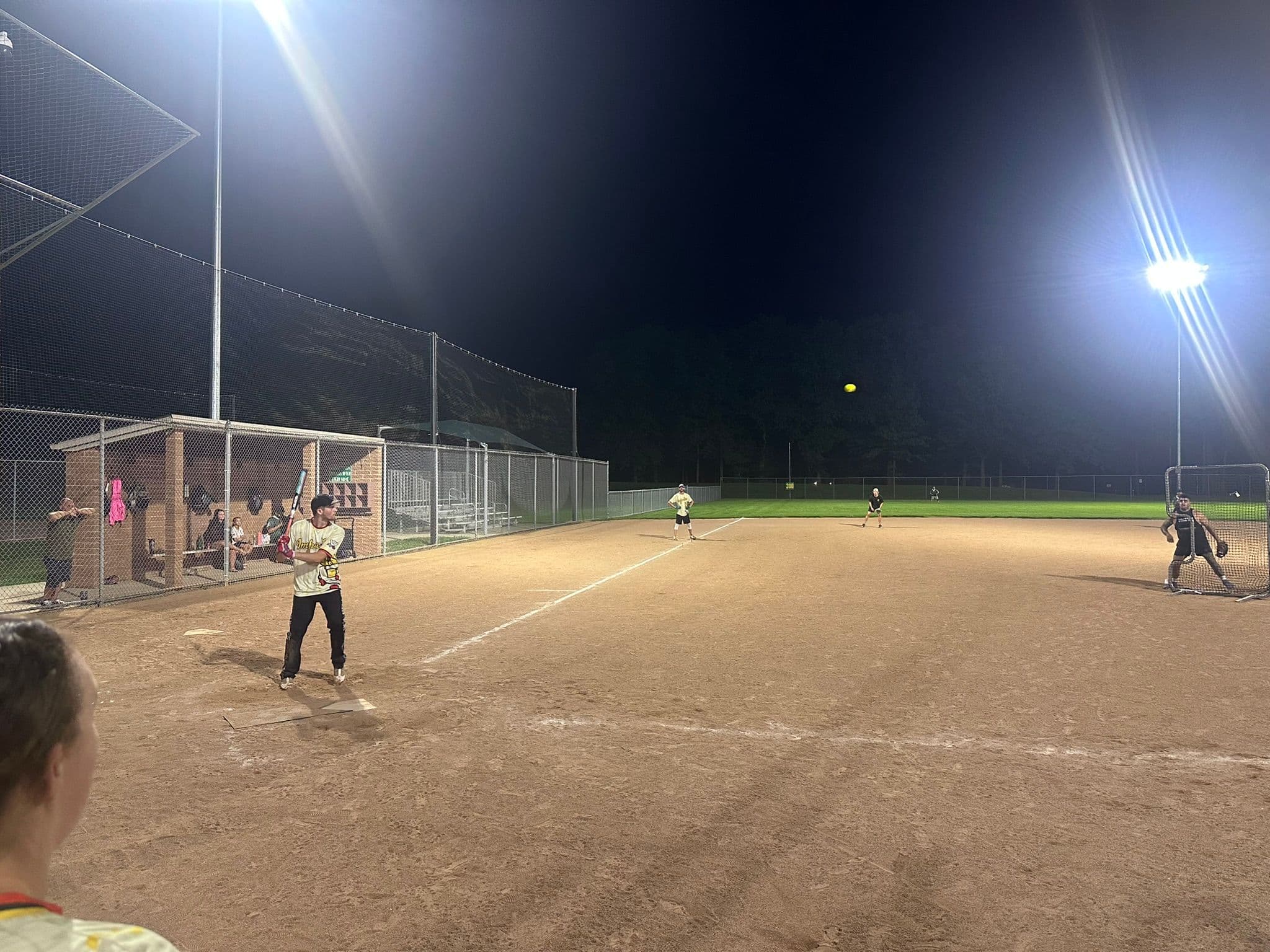 Kyle Liddle at the plate in the cream Impastas jersey with the pitch in the air, the pitcher's screen and the pitcher at the right of frame