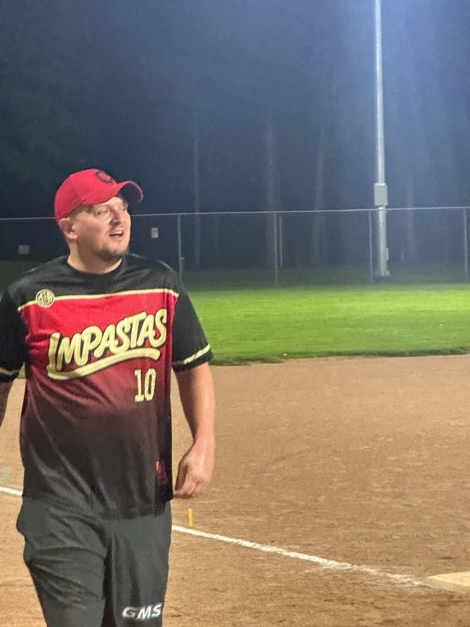 Cody Dye in the new red and black Impastas jersey, number 10, and a red cap, walking in off the infield dirt under the lights